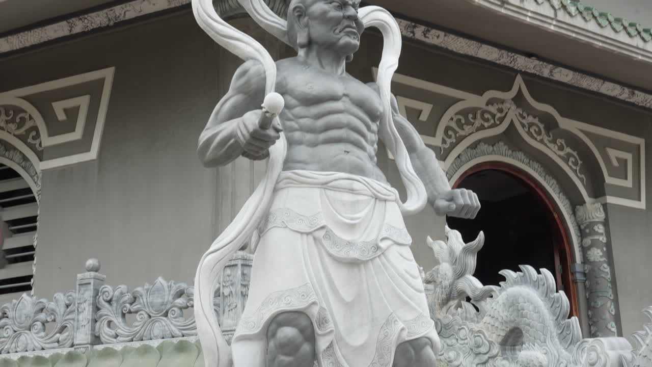 A towering stone statue of a muscular warrior stands in Vietnam, with detailed carvings
