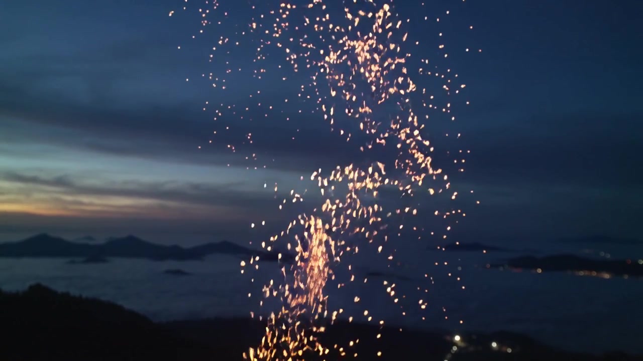 Fontana dorata scintillante che si attorciglia verso l'alto, poi disperdendo braci sopra la cima di una collina al tramonto, illuminando il mare.