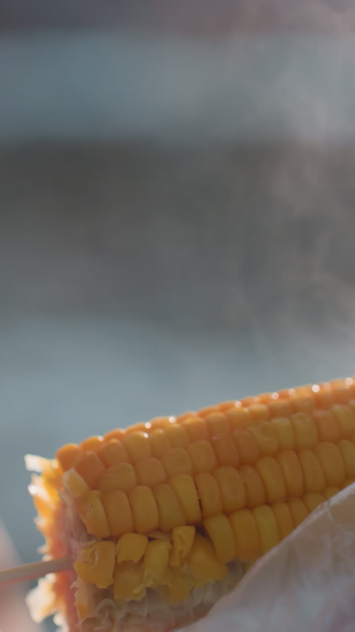 up de persona girando maíz mientras el vapor se eleva de maíz recién cocido, al aire libre, fondo borroso que muestra el ambiente frío de invierno, bocadillo caliente saludable, calor en clima frío
