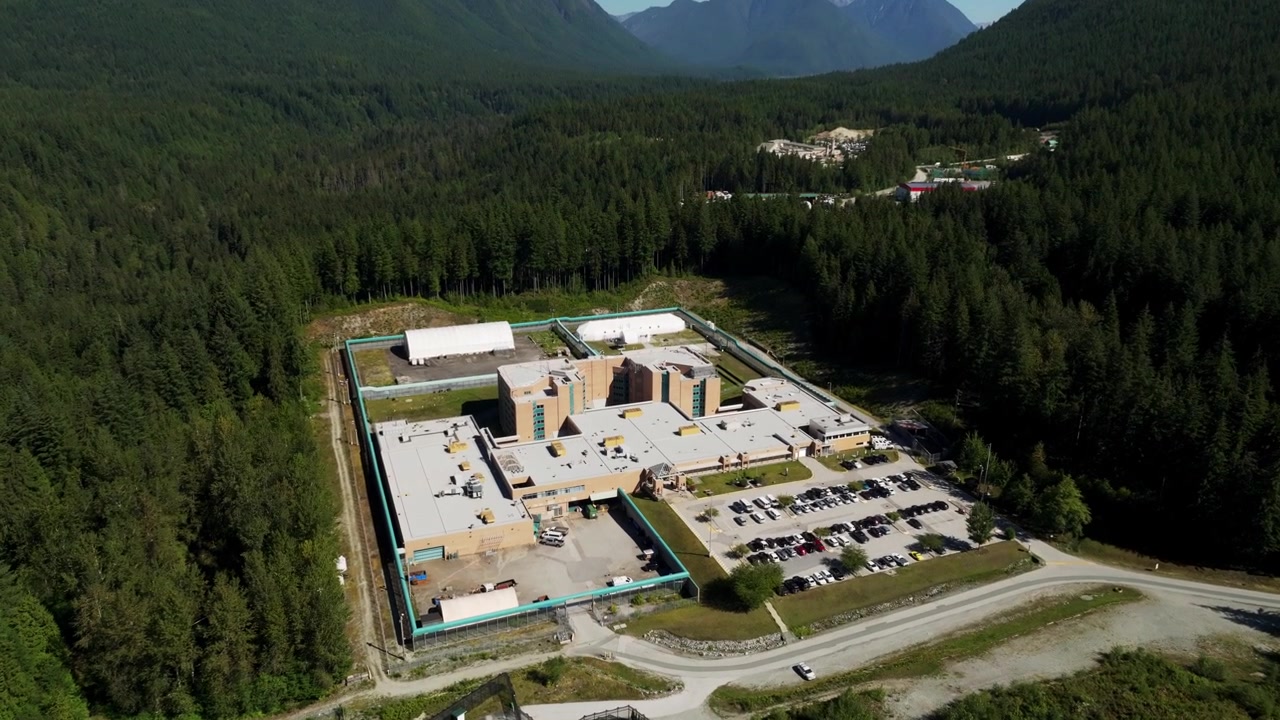 Fraser Regional Correctional Centre, Maple Ridge, British Columbia, Canada - Et fængsel omgivet af tæt skov, med bjergtoppe i baggrunden - Drone flyver fremad.