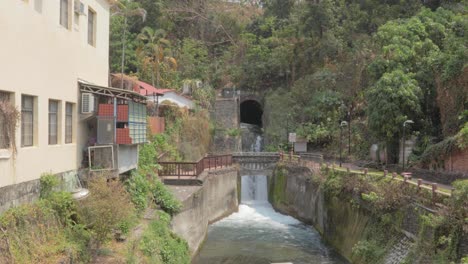 A-waterfall-spouting-out-water-from-the-side-of-a-hill-and-into-a-canal-in-a-small-village-in-southern-Taiwan---wide-shot