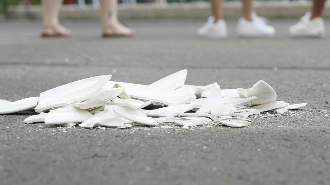 Broken ceramic pieces on asphalt with people walking in the background