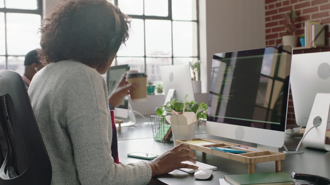 joven programadora afroamericana codificando software de seguridad de red para una empresa de inicio desarrollador web profesional escribiendo código en la pantalla de la computadora bebiendo café en una oficina de inicio moderna