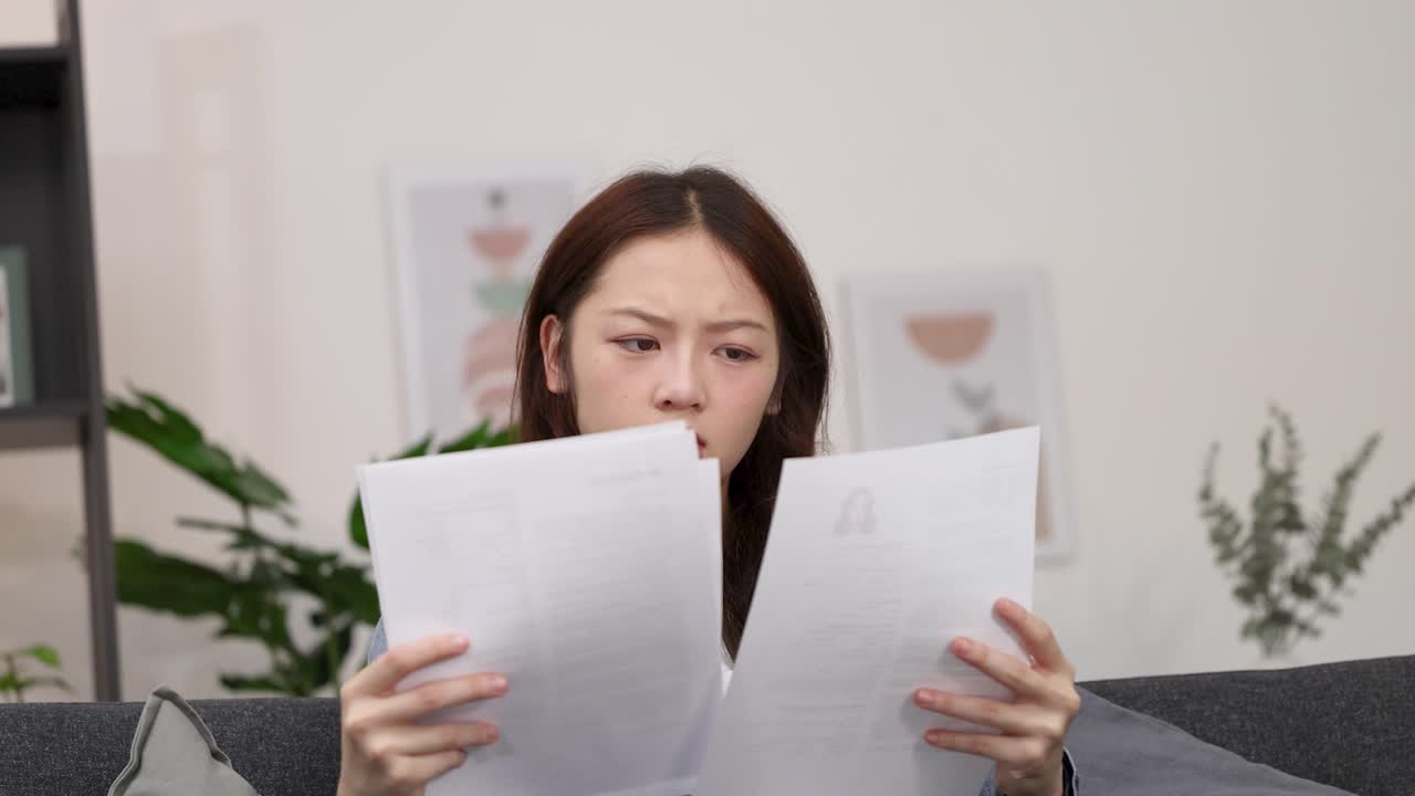 A young Asian woman in a denim jacket carefully reads documents with a focused expression