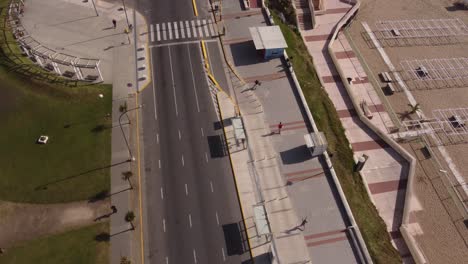 Aerial-trakcing-shot-of-runner-running-on-beach-promenade-beside-road-during-sunny-day-in-Mar-del-Plata-City,Argentina