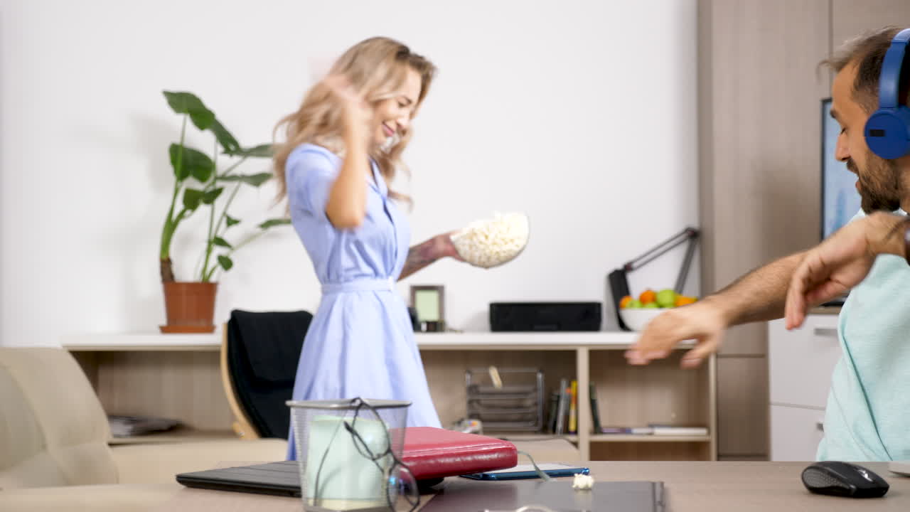 Man working on laptop with woman eating popcorn in the background