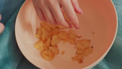 close up of woman hand with long nails reaching for popcorn in blue bowl placed on soft teal blanket, scene suggests relaxing indoor moment