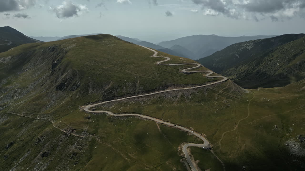 A breathtaking view of Transalpina's serpentine roads in Romania, enveloped by verdant mountainsides and punctuated with cloud shadows