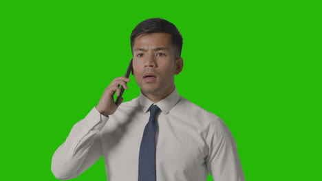 studio shot of serious businessman in shirt and tie talking on mobile phone against green screen