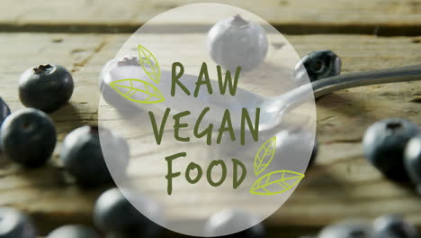 animación de un cartel de texto de comida vegetariana cruda contra un primer plano de bayas azules y cuchara en una mesa de madera