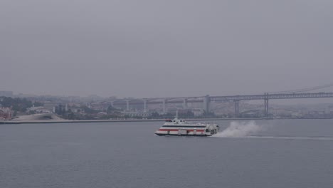 ferry glides across the tagus river in lisbon on an overcast day, bridge in the background