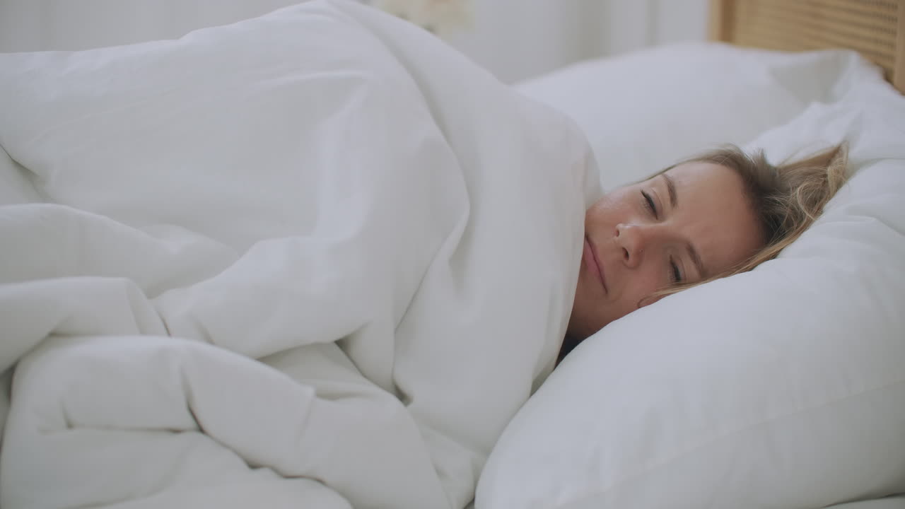 젊은 여성이 침실에서 침대에 누워있어 얼어붙고 추운 계절에 중앙 난방 문제가없는 집에서 추위를 느 ⁇ 다. 아픈 아픈 소녀는 담요에 싸여 열을  ⁇ 고 독감 증상이 있습니다.