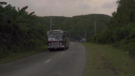 a bus driving down a small country road in cuba surrounded by mountainous forests