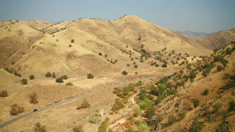 Un-Coche-Solitario-Conduce-Por-Una-Carretera-Solitaria-En-Un-Cañón-Entre-Altas-Montañas-Desérticas-En-El-Sur-De-California---Vista-Aérea