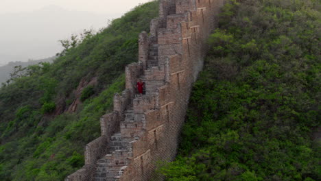 Una-Persona-De-Rojo-Está-Subiendo-Los-Escalones-De-Un-Largo-Muro-De-Piedra-Que-Cruza-La-Montaña