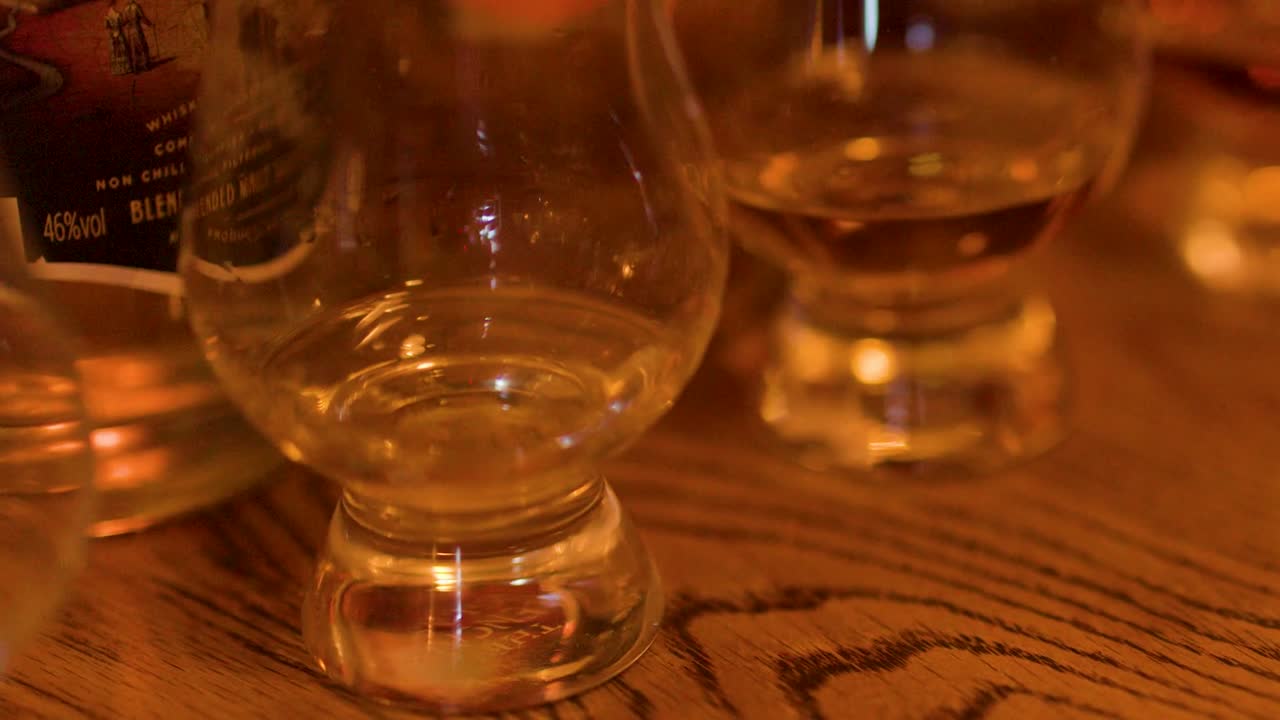 Una luz ambiental cálida ilumina unas copas de cata de cristal vacías sobre la superficie texturizada de una barra de madera.
