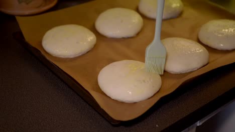 close-up of a female brushing wiped egg on top of the the buns, preparing them for the oven