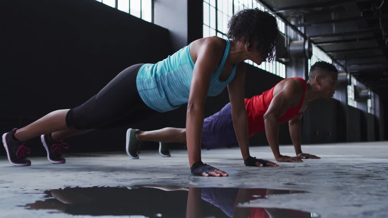 African american man and woman doing push ups in an empty urban building