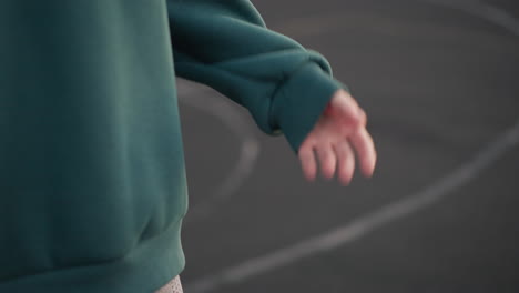 primer plano de una persona con capucha verde agitando las marcas de la mano en el suelo, preparándose para el servicio de voleibol con enfoque en el movimiento de la mano y las marcas de entrenamiento en la cancha deportiva al aire libre