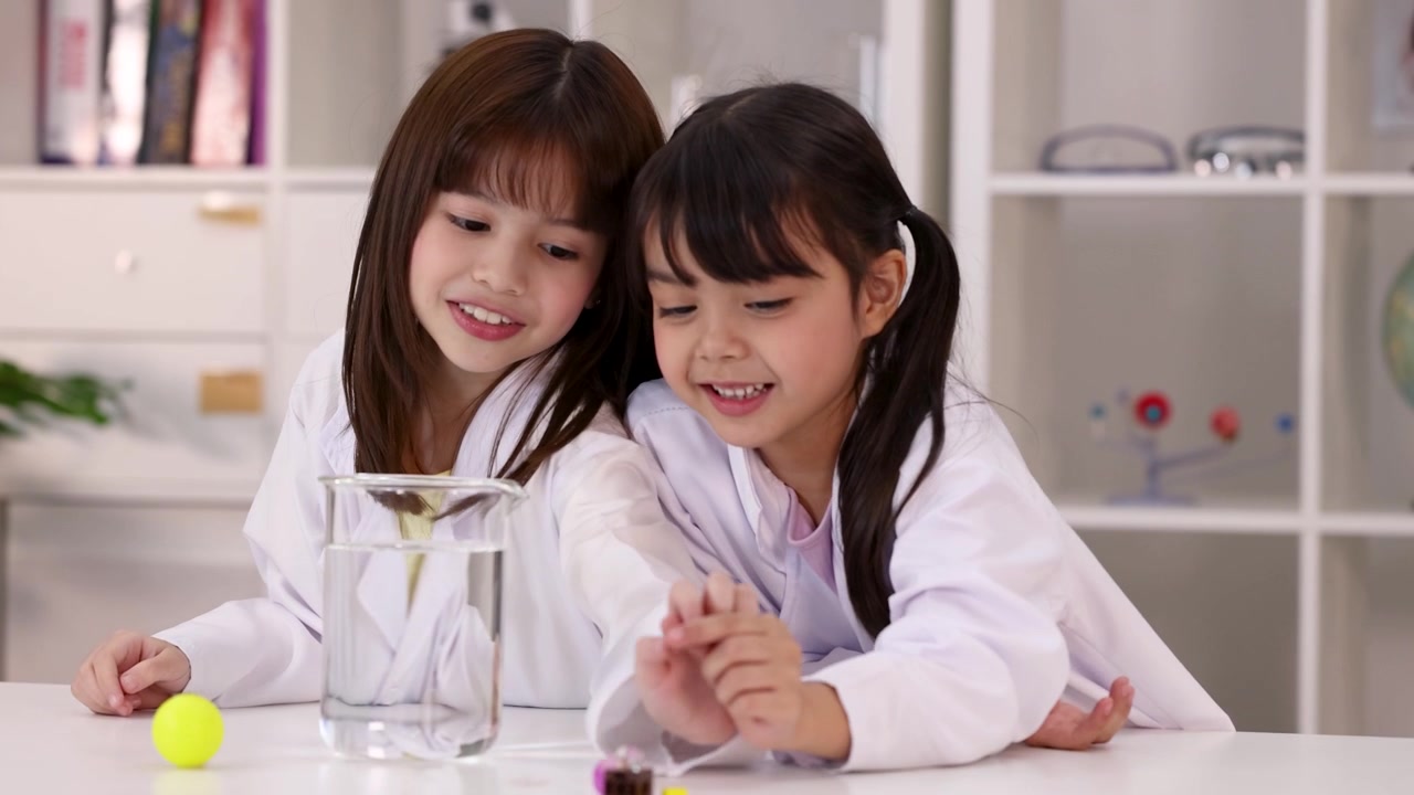 小學生穿著白色實驗袍，在STEM科學課堂中觀察一個水燒杯。