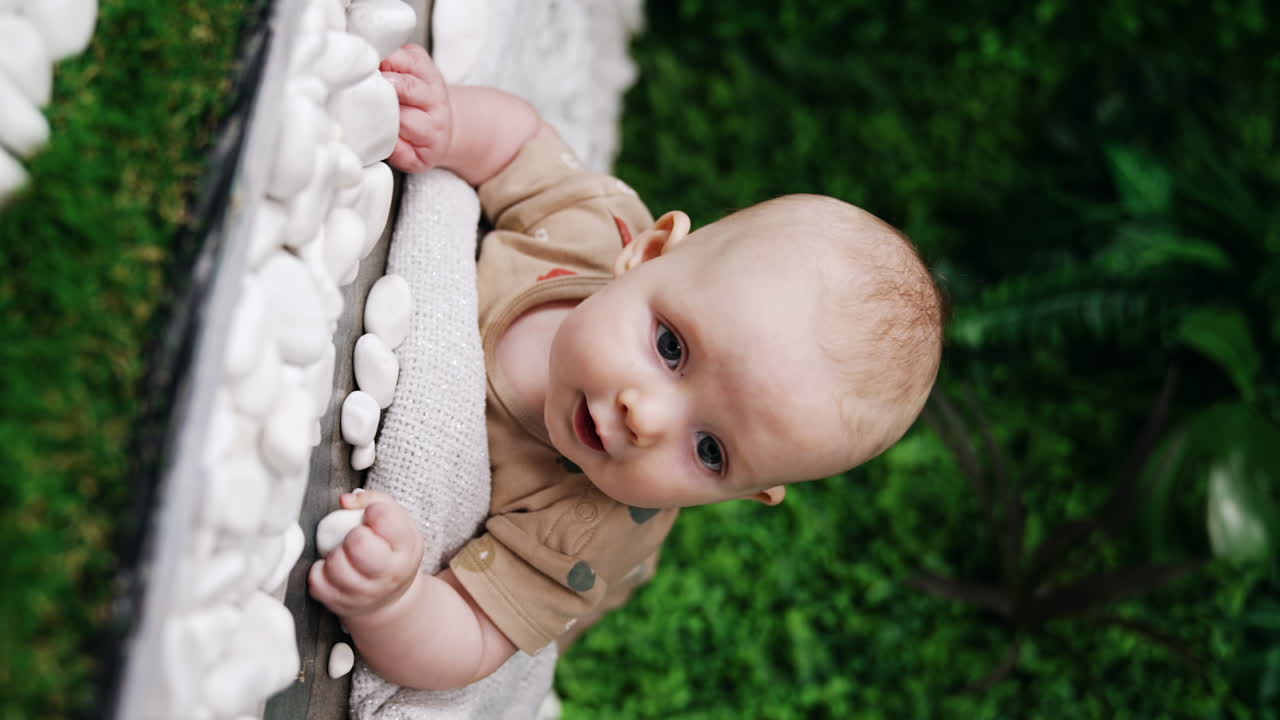 Lovely baby boy lies on the plaid on his belly. Smiling Caucasian infant looks up with a smile. Vertical screen.