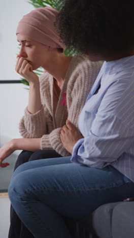 vertical video of upset young woman patient wearing headscarf receiving chemotherapy treatment for breast cancer being comforted by female patient