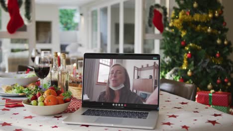 feliz mujer caucásica con máscara facial en una computadora portátil acostada en la mesa de navidad