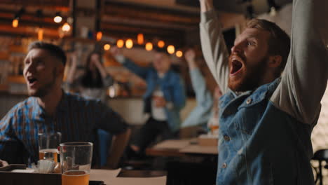 close-up of a group of fans of men and women sitting together in a bar and watching a broadcast on tv enjoying a goal scored shouting and hugging. in football basketball.