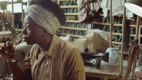 thoughtful african american woman sitting in shoemaker workshop