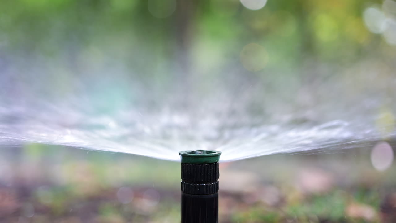 Close up of a water sprinkler in action, spraying water across grass and plants