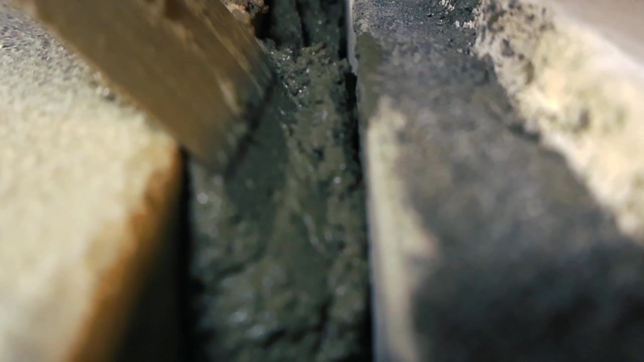 Extreme close up of a construction worker meticulously applying wet cement mortar into the gaps between stones, expertly leveling the screed mixture for a new floor foundation