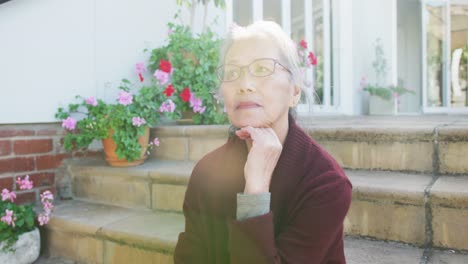 Happy-asian-senior-woman-sitting-on-stairs-on-sunny-day-in-garden