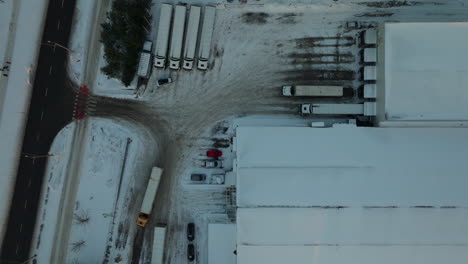 Vista-Aérea-De-Pájaro-Del-Estacionamiento-Del-Edificio-De-Logística-De-Distribución-Cubierto-De-Nieve-En-Dabrowa,-Polonia