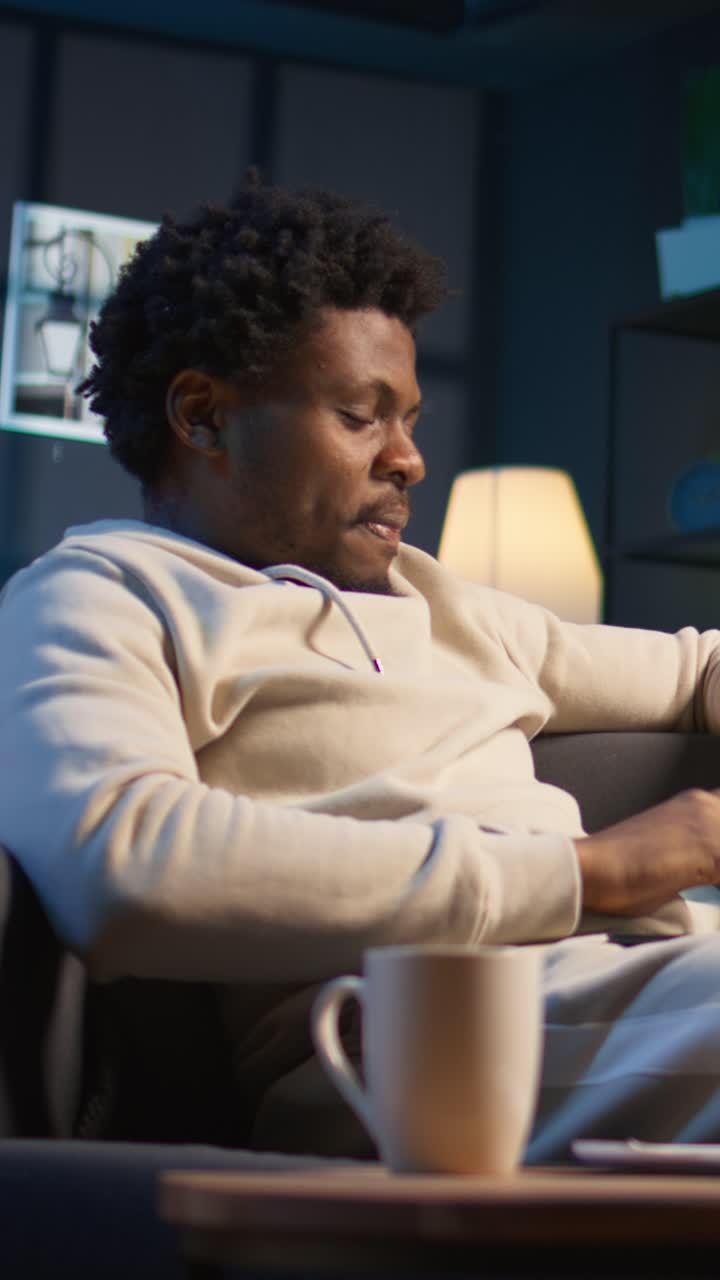 Ung afroamerikansk mand slapper af i sofaen og drikker kaffe