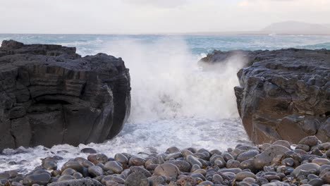 las olas se estrellan contra columnas de basalto volcánico en una playa de guijarros en islandia, creando una dramática escena natural.