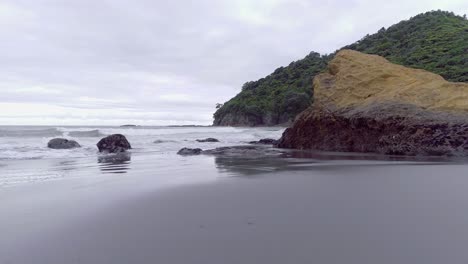 flying low past rocky jagged cliffs on beach in new zealand, cloudy day