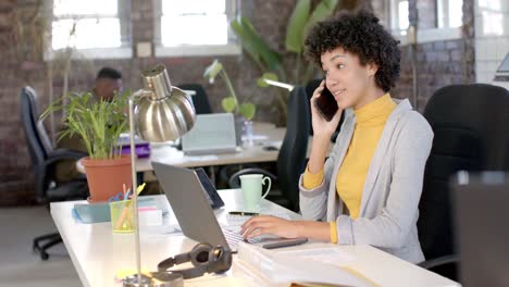 Happy-biracial-casual-businesswoman-talking-on-smartphone-in-office-in-slow-motion