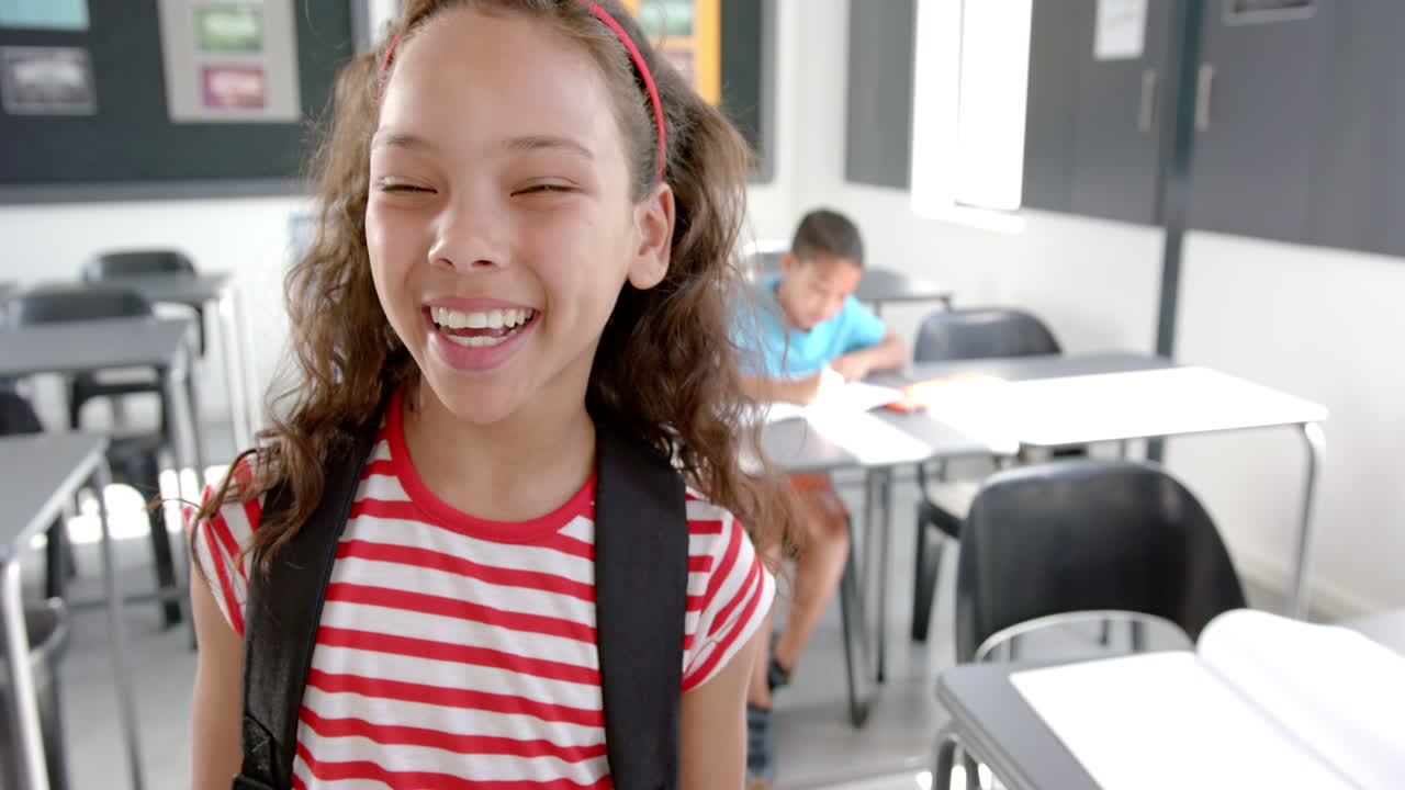 Biracial girl in striped shirt stands in a classroom, joyful