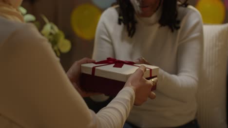 woman giving female friend birthday present at home with party balloons in background 1