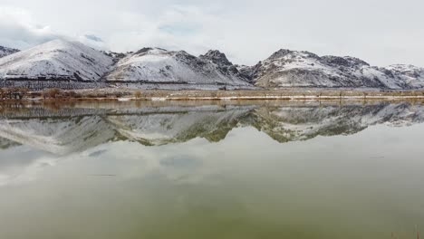 Aerial-drone-shot-of-rural-Diaz-Lake-and-snowy-mountain-range-in-backdrop-during-sunlight---California-,America