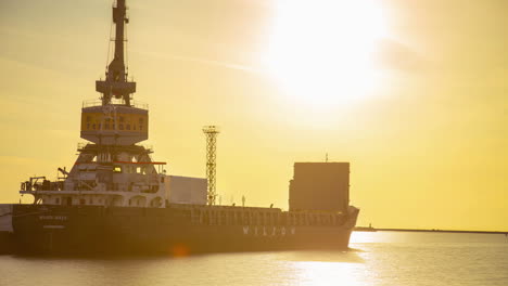 Ein-Kran-Lädt-Bei-Sonnenuntergang-Schiffscontainer-Auf-Einen-Lastkahn---Zeitraffer