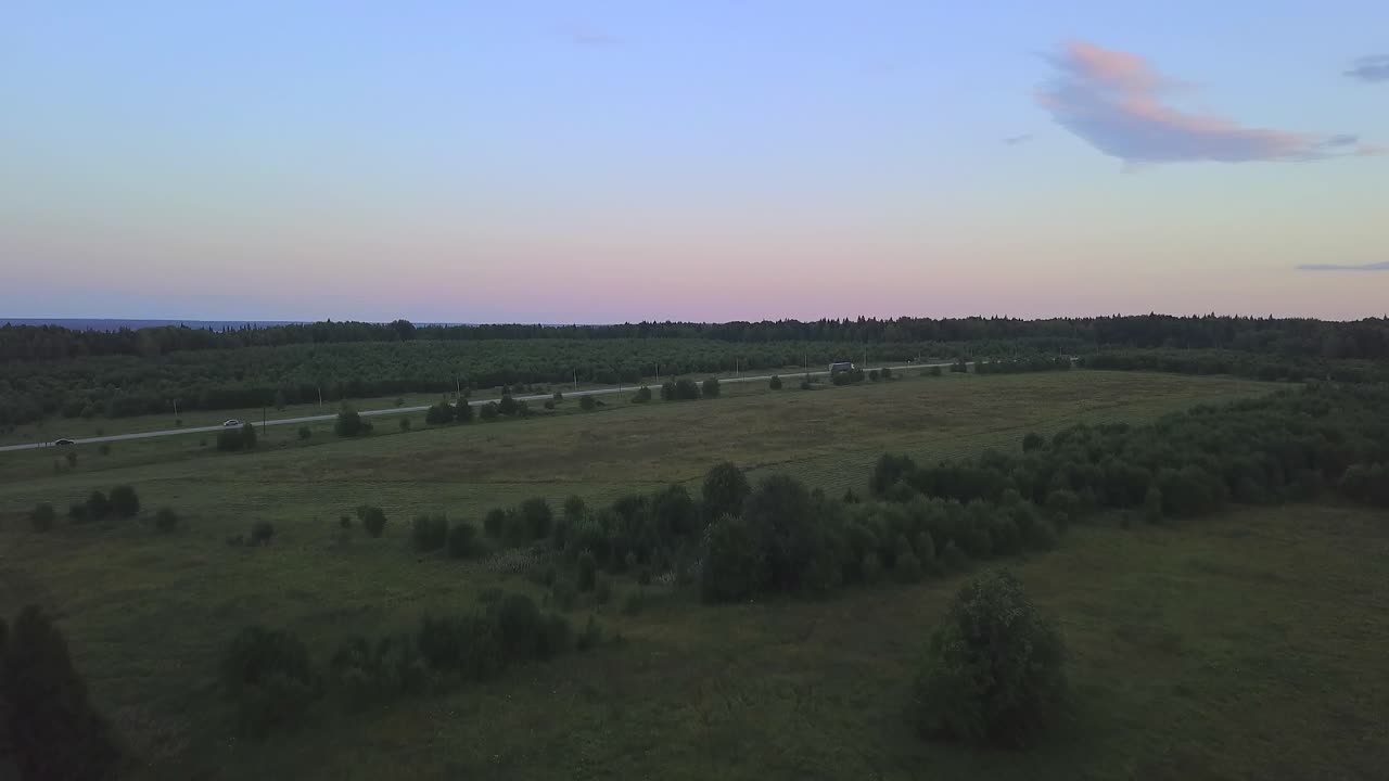 Solnedgang over landlig landskap med vei og skog