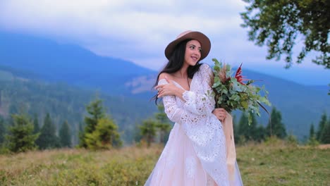 Sexy bride in wedding dress in the mountains. Smiling young girl in hat and white dress proudly stands on mountain background.