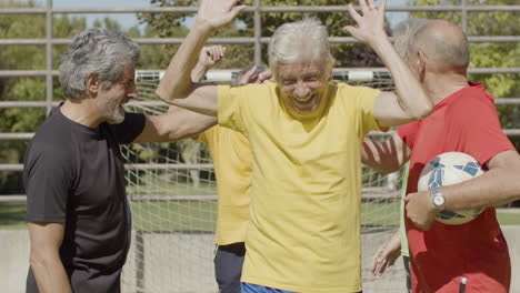 front view of happy senior football players celebrating victory, raising their arms and running on the pitch