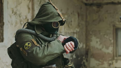 a man in an abandoned building looking at the readings on his arm he was wearing a gas mask and prot