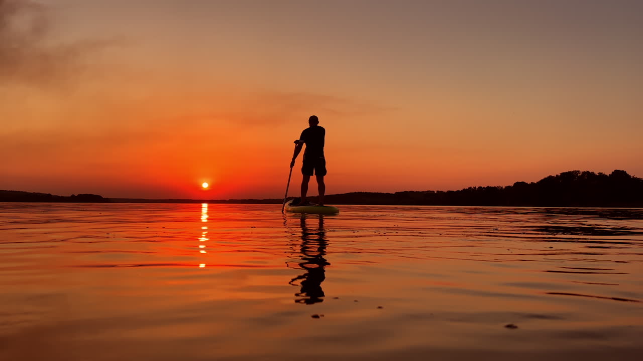 Active time spending in the summer evening time. Male sup boarding on the river at sunset.
