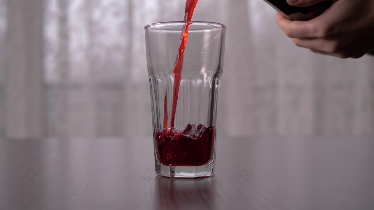 Versamento di succo di ribes nero in un bicchiere alto al rallentatore, ripresa frontale