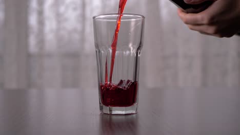 Pouring-blackcurrant-juice-into-tall-glass-in-slow-motion,-straight-ahead-shot