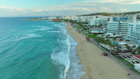 Costa-De-Playa-De-Arena-En-Protaras-Con-Complejos-De-Hoteles-De-Lujo-Frente-Al-Mar-Al-Atardecer,-Chipre---Retroceso-Aéreo