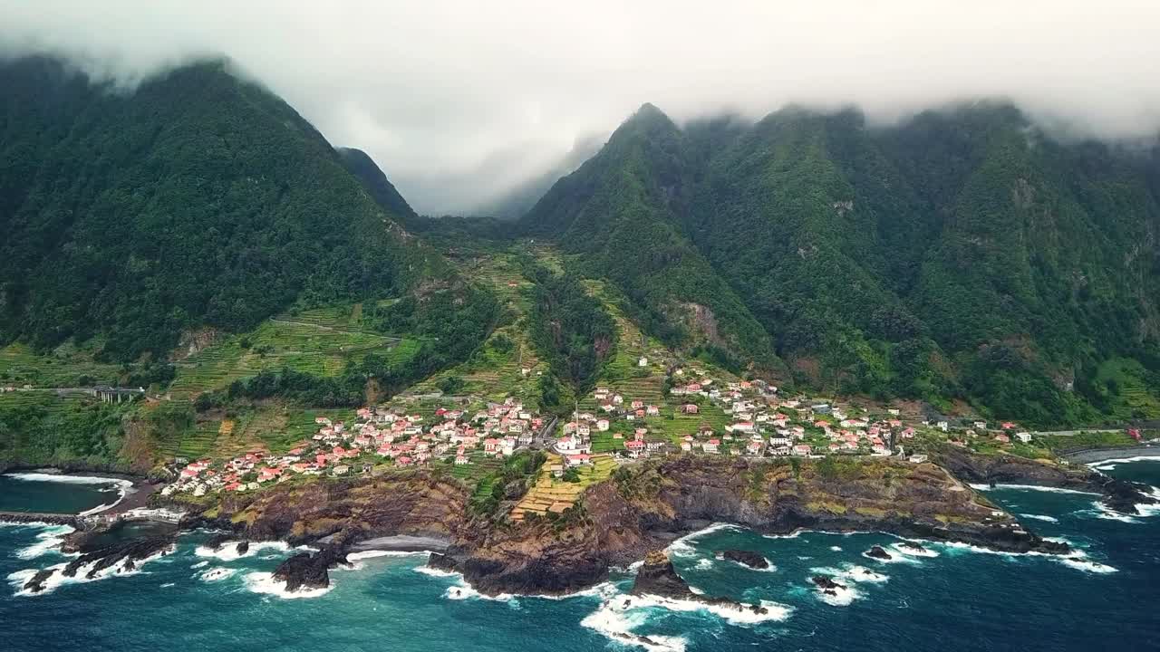 Breathtaking aerial view of Seixal, a picturesque coastal village in Madeira, highlighting natural lava pools and powerful Atlantic waves crashing against rugged cliffs, slow motion drone shot
